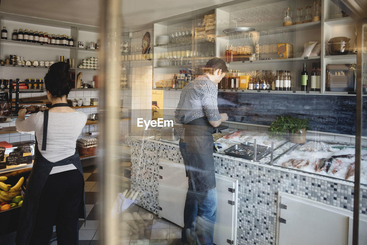 Rear view of owners working in fish store seen through glass