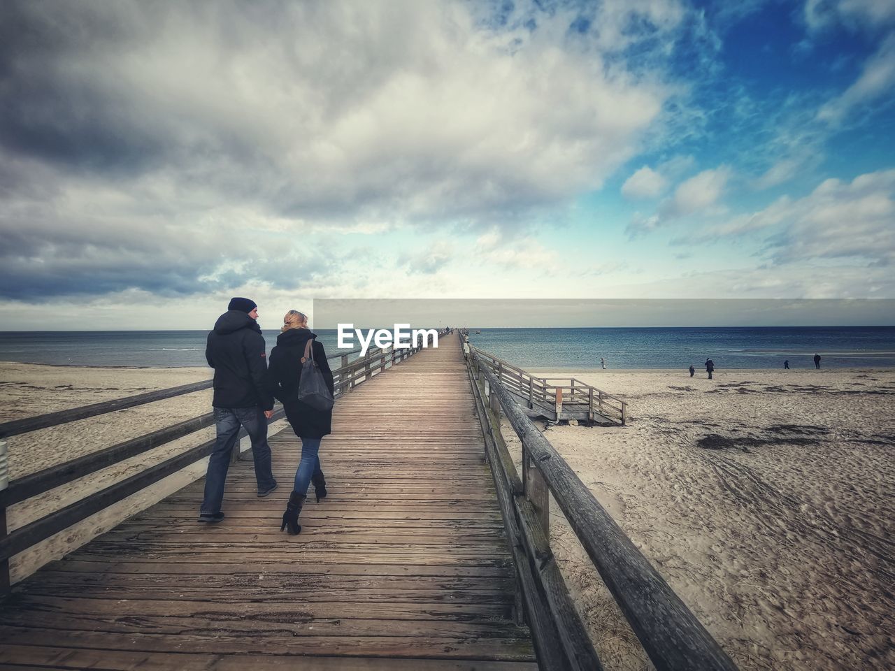 REAR VIEW OF MEN WALKING ON BEACH AGAINST SKY