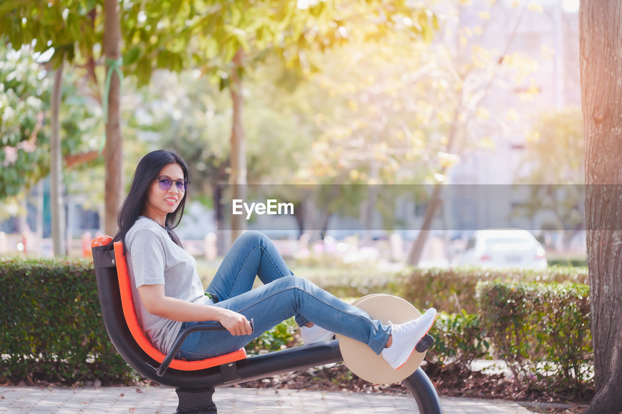 PORTRAIT OF SMILING YOUNG WOMAN SITTING ON PLANT