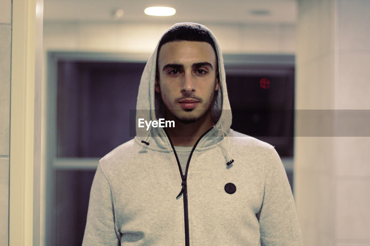 Portrait of young man standing in illuminated corridor