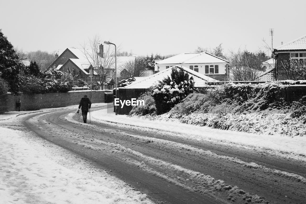 Rear view of man walking on snow covered street against houses in winter