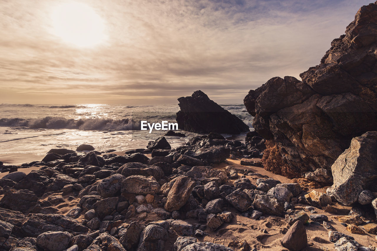 SCENIC VIEW OF ROCKS AT BEACH AGAINST SKY DURING SUNSET