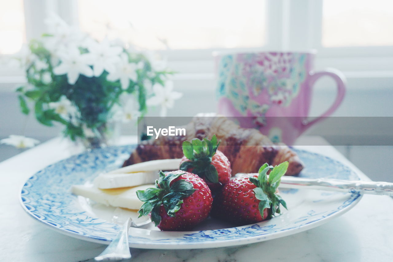 Croissant and strawberries with cheese in plate on table