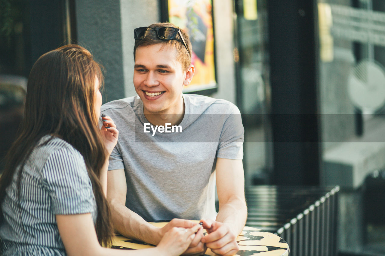 Happy man looking at girlfriend at outdoor cafe in city