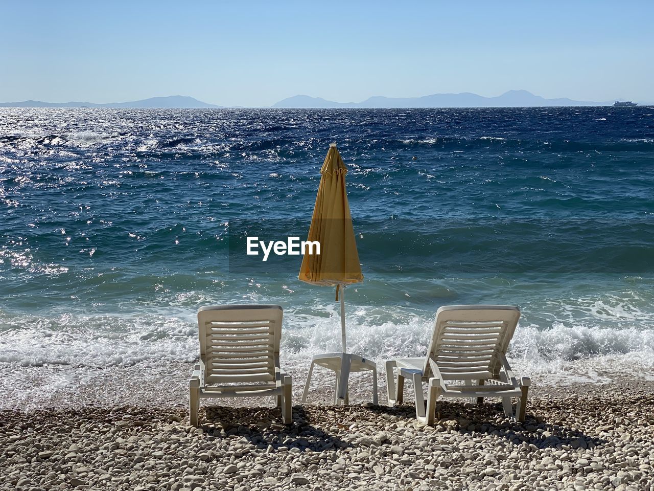 EMPTY CHAIRS ON BEACH AGAINST SKY