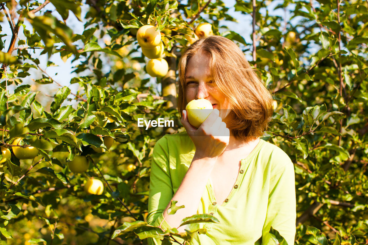 Portrait of woman holding apple against tree