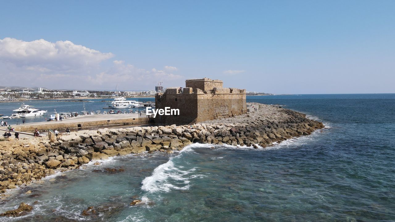 water, sea, sky, coast, architecture, land, beach, shore, ocean, built structure, tower, nature, breakwater, travel destinations, building exterior, scenics - nature, vacation, building, history, cliff, fort, the past, travel, body of water, beauty in nature, horizon over water, blue, coastline, day, tourism, horizon, wave, no people, terrain, rock, castle, outdoors, holiday, cove, motion, lighthouse, clear sky, bay, sunny, cloud, trip, tranquil scene, tranquility, wall, sunlight