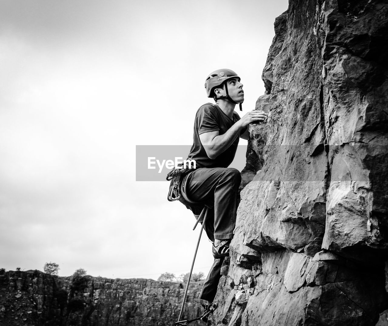 Full length of young man rock climbing against sky