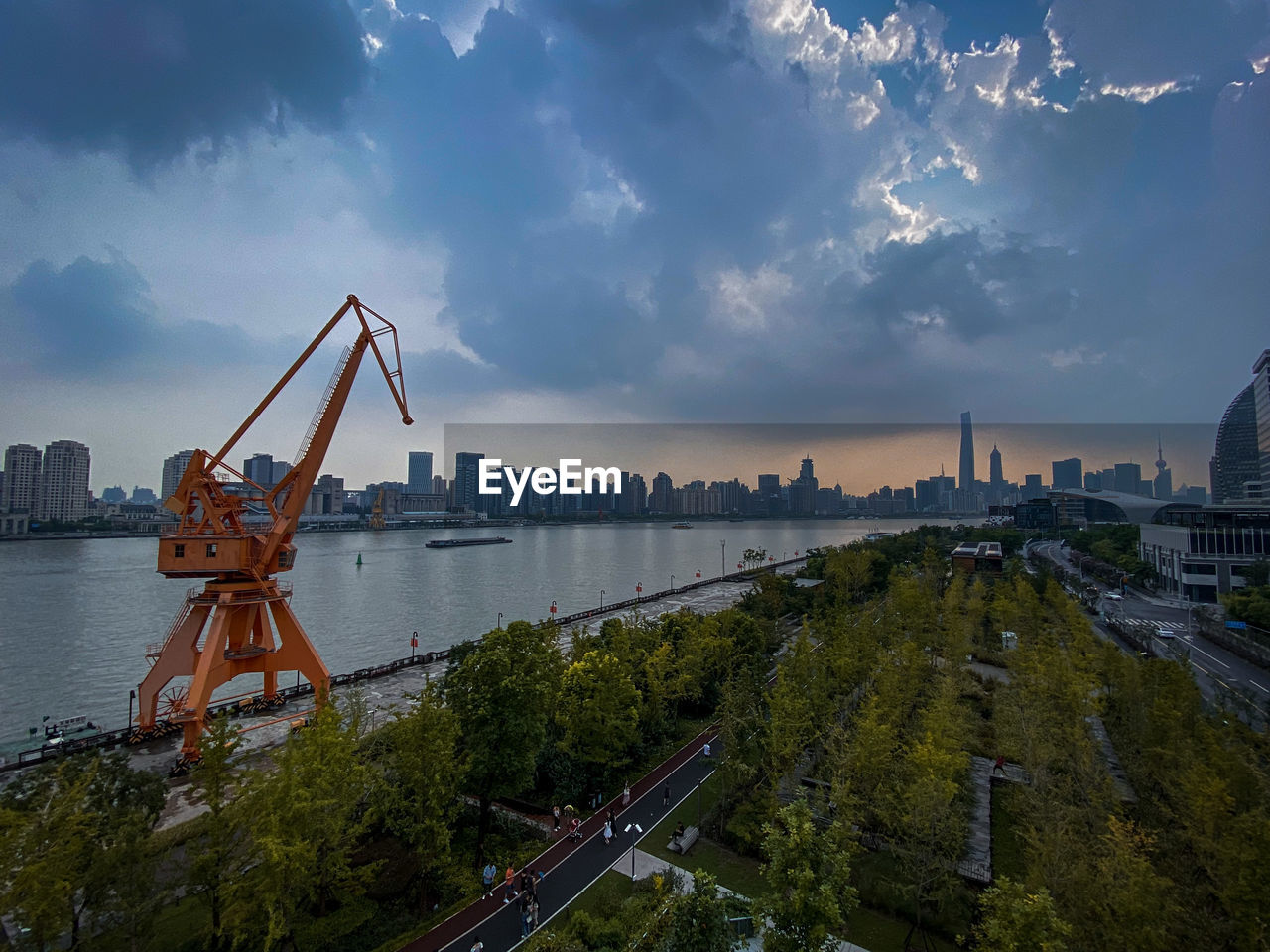 CRANES BY RIVER IN CITY AGAINST SKY