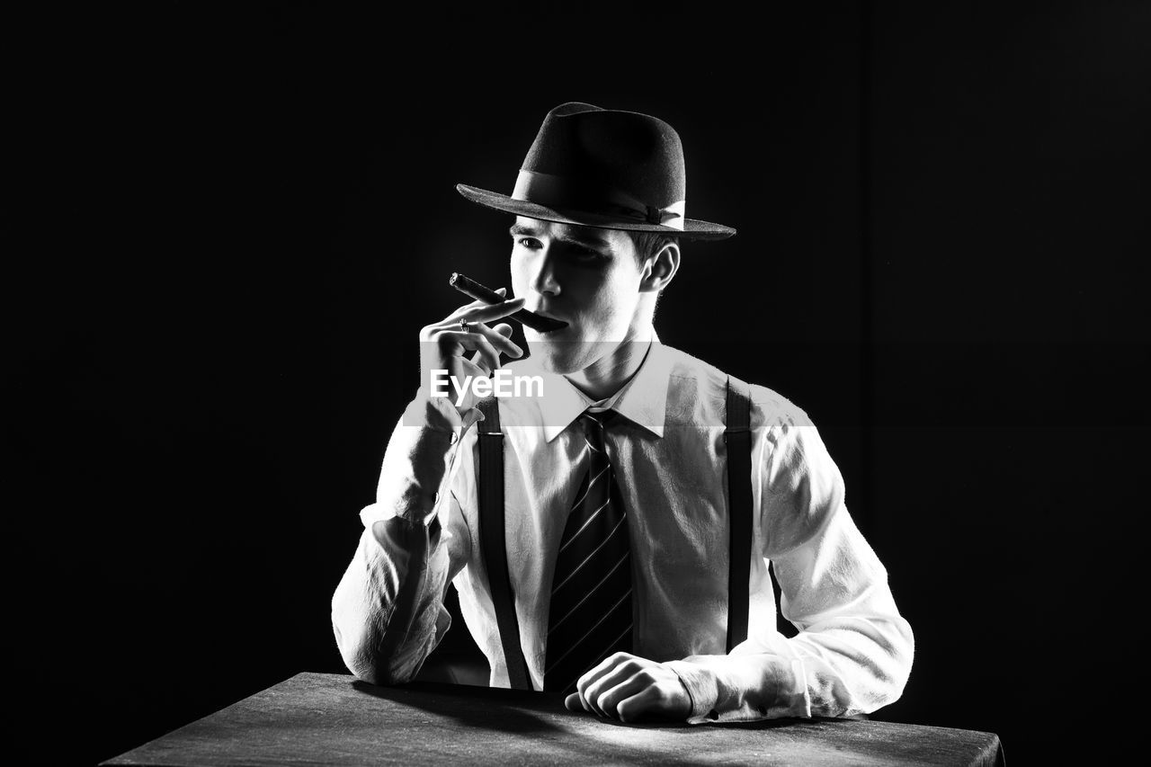 Young man smoking cigar against black background