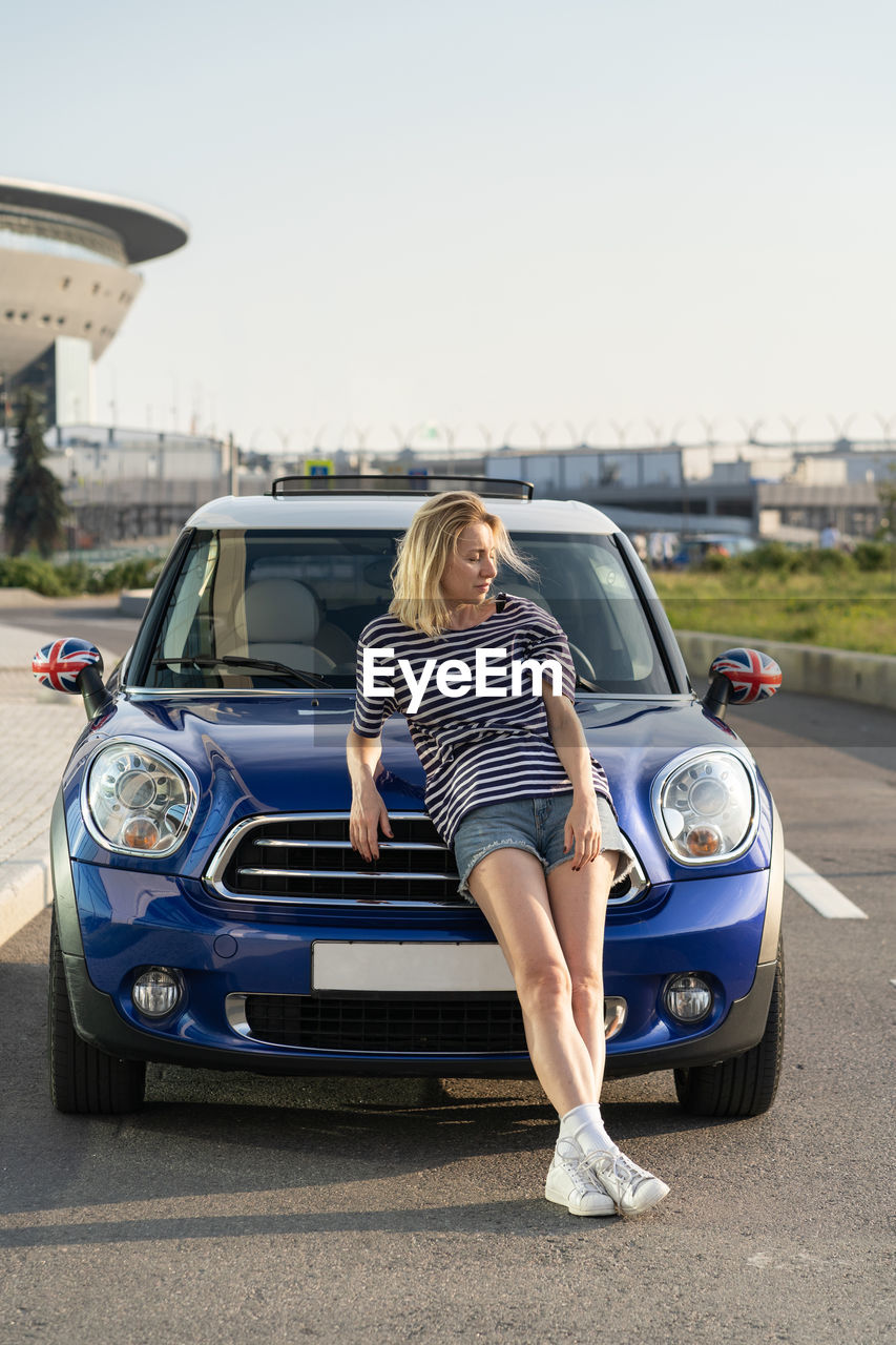 Confident woman auto owner at modern car outside urban buildings of automobile dealership center