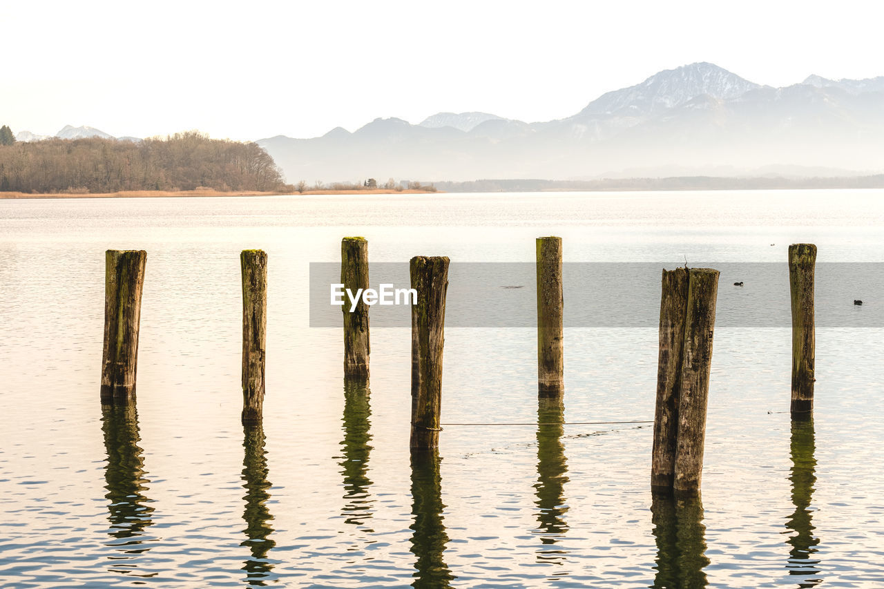 Wooden posts in lake against sky