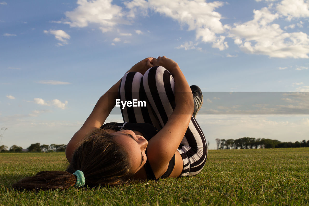 Woman lying on grass against sky