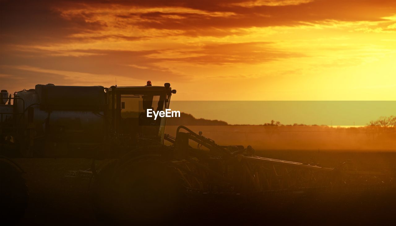 Agricultural machinery on field against sky during sunset
