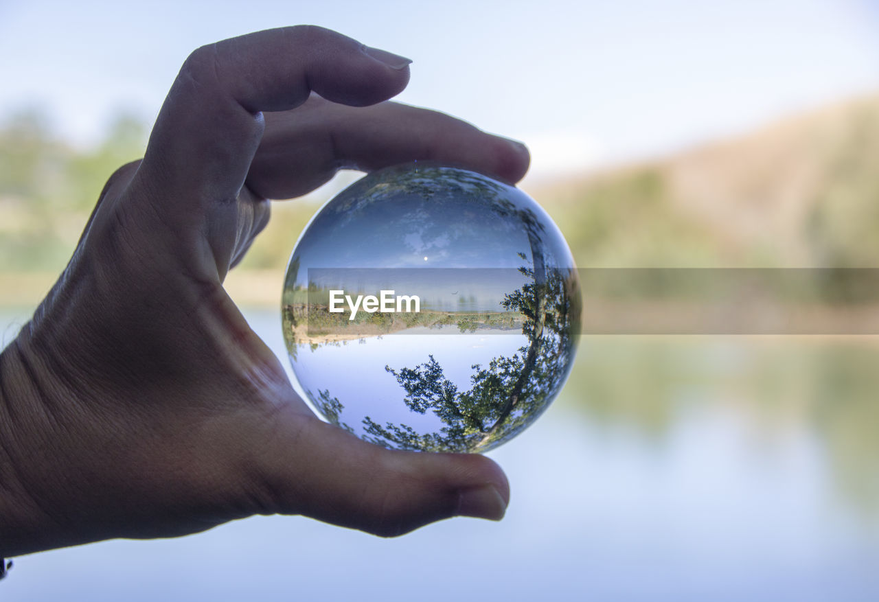 Cropped image of person holding crystal ball against lake