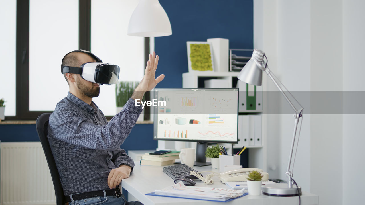 Young businessman wearing virtual reality simulator gesturing with hand