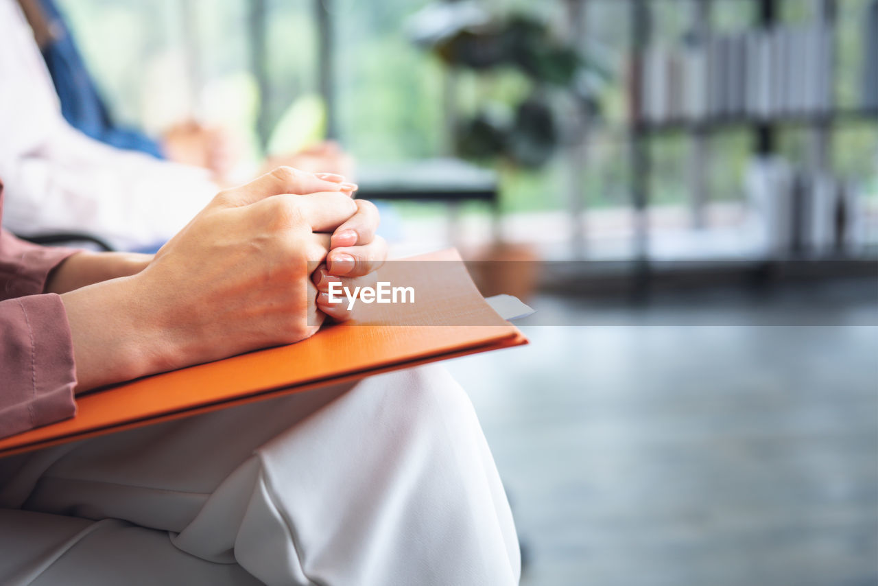 midsection of woman holding book while sitting on table