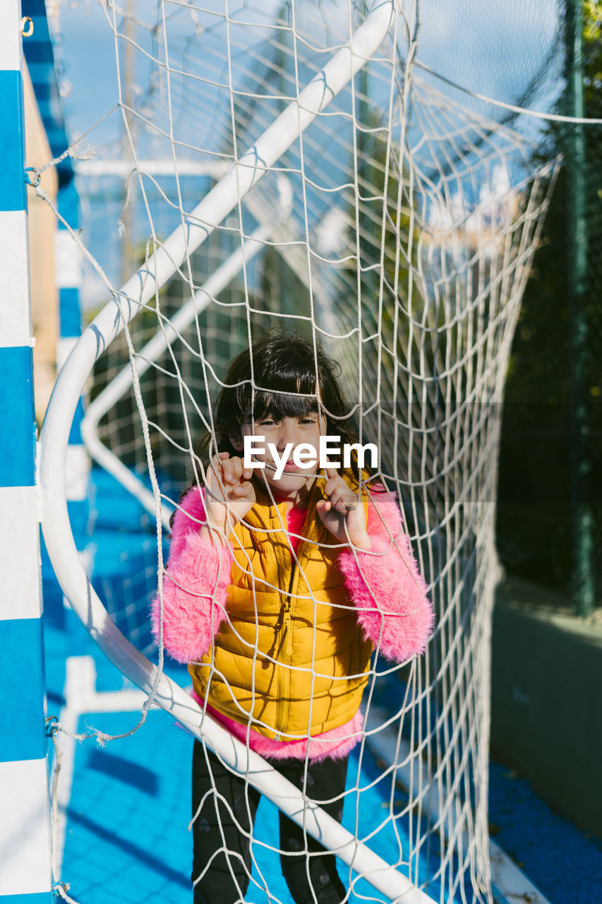 Cute girl leaning on goal post net at soccer court during sunny day