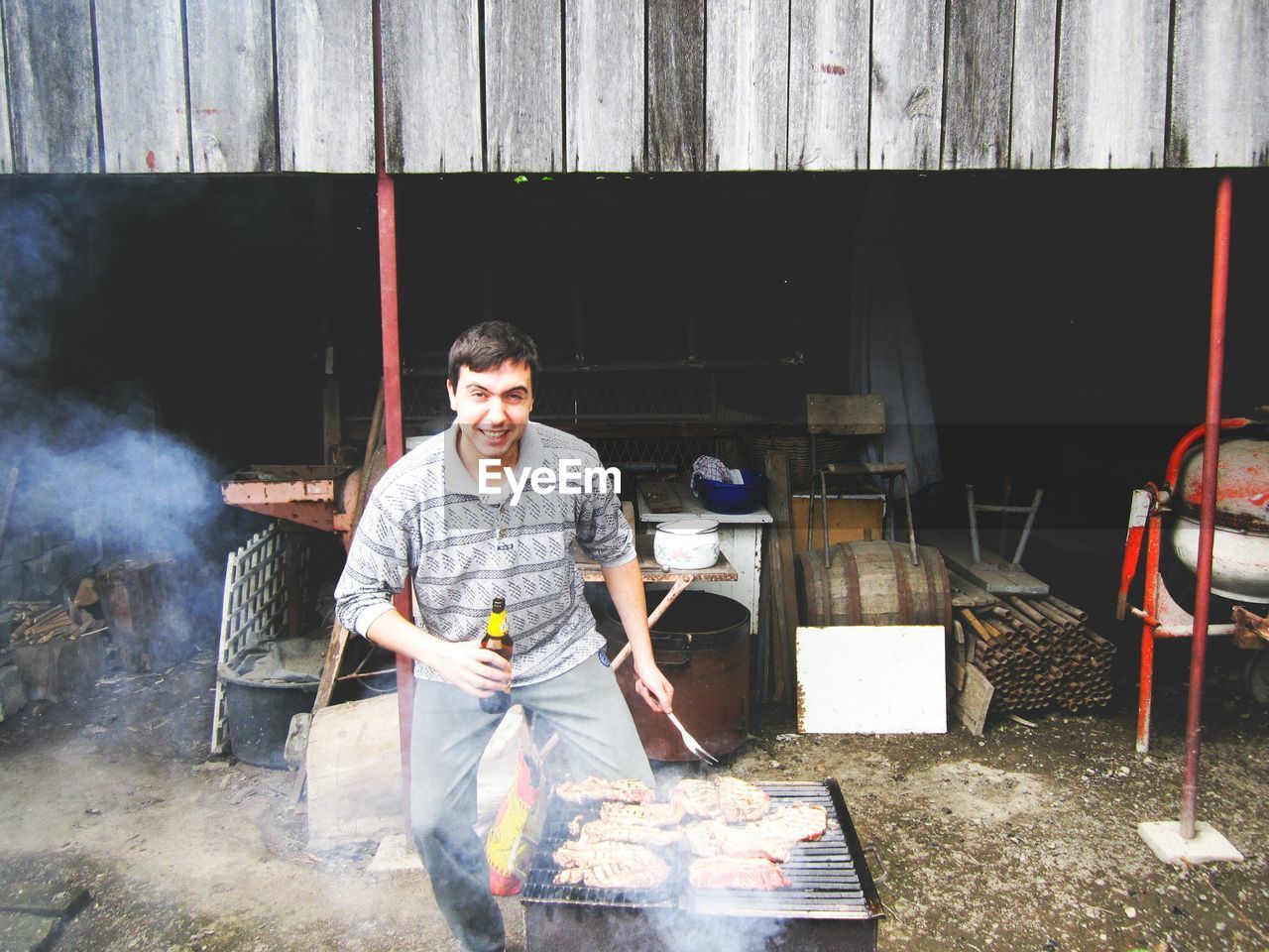 Portrait of smiling man cooking barbecue grill while standing against yard