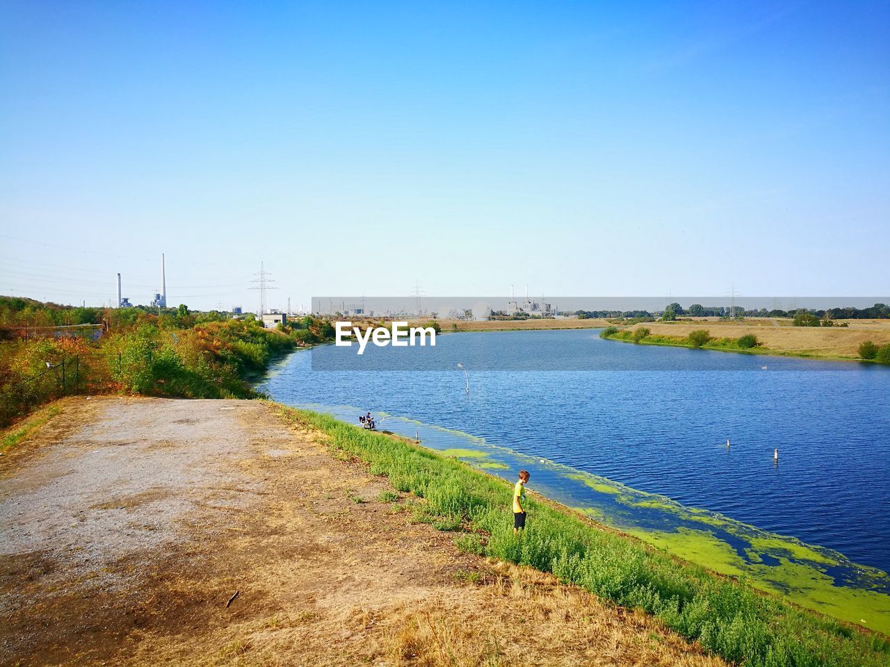 Boy standing by river against clear blue sky