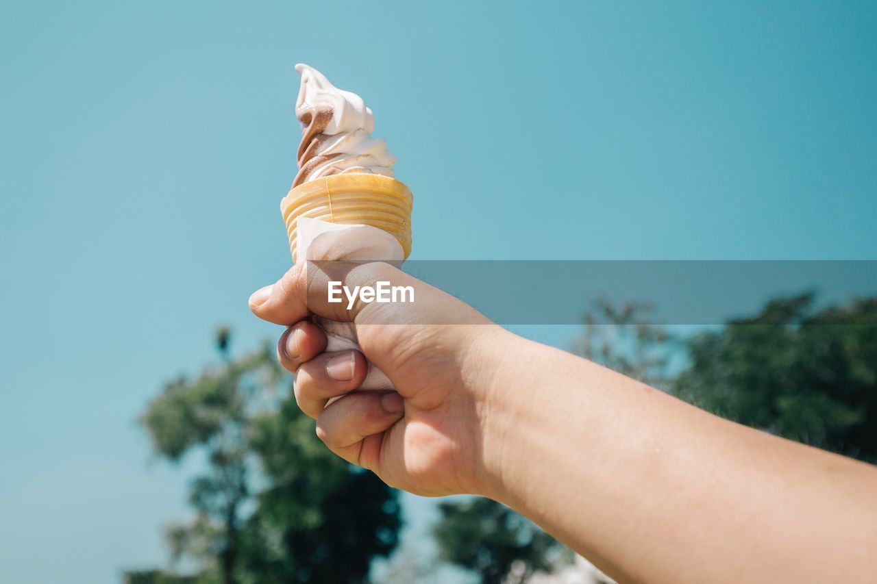 Close-up of hand holding ice cream against sky