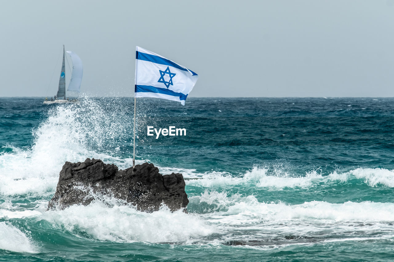 Scenic view of rock with flag in sea against clear sky