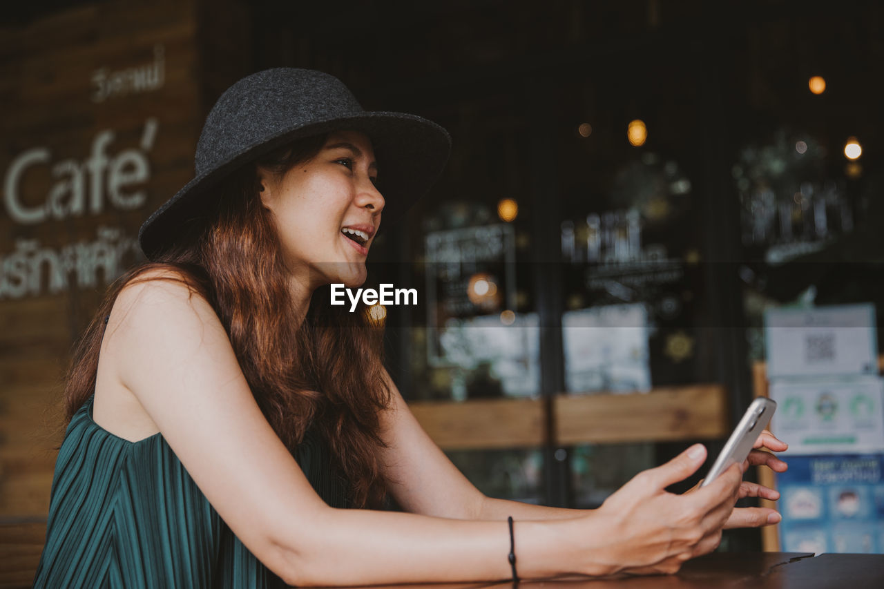 PORTRAIT OF YOUNG WOMAN USING MOBILE PHONE AT CITY