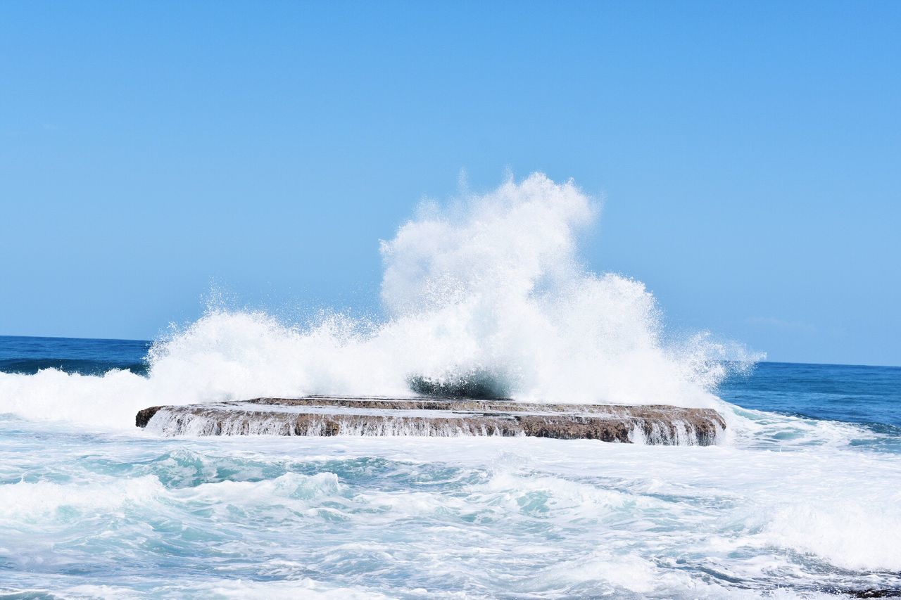 Waves splashing on shore against clear blue sky