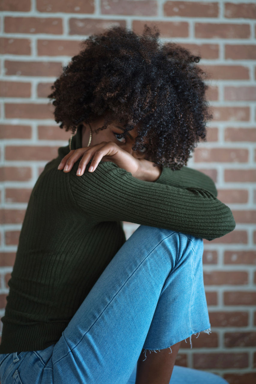 Beautiful black woman with afro hair sitting on the chair against the brick wall background