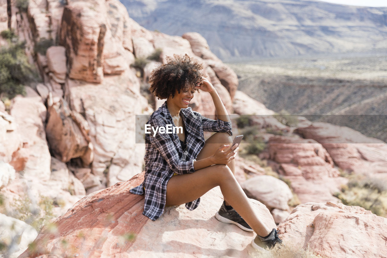 Woman using smart phone while sitting on rock formation