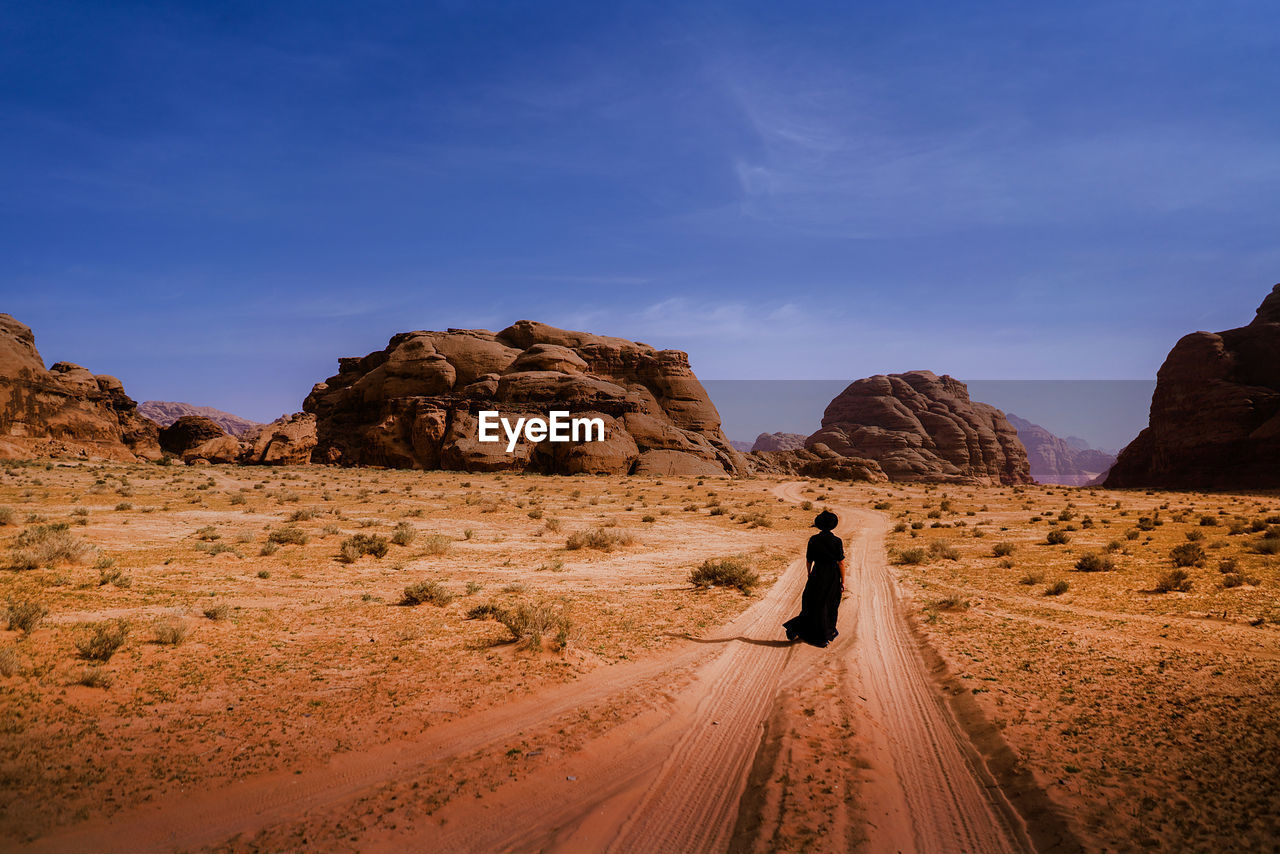 Rear view of woman walking on dirt road against sky