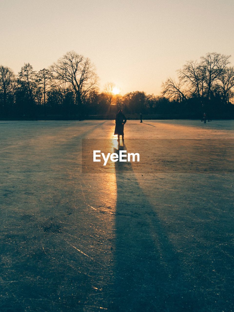 Woman standing on frozen lake against sky during sunset