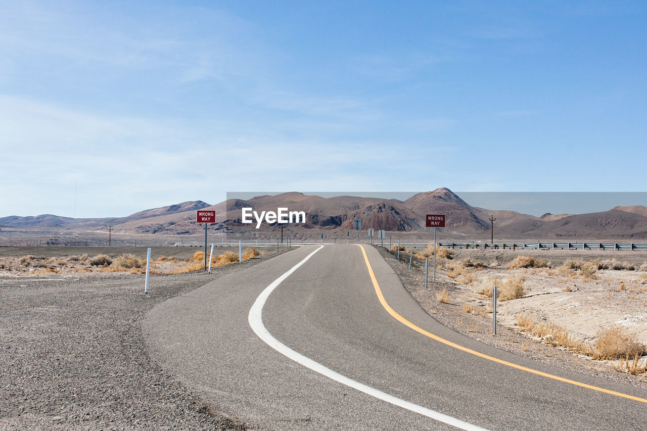 Empty road leading towards mountains against sky on sunny day