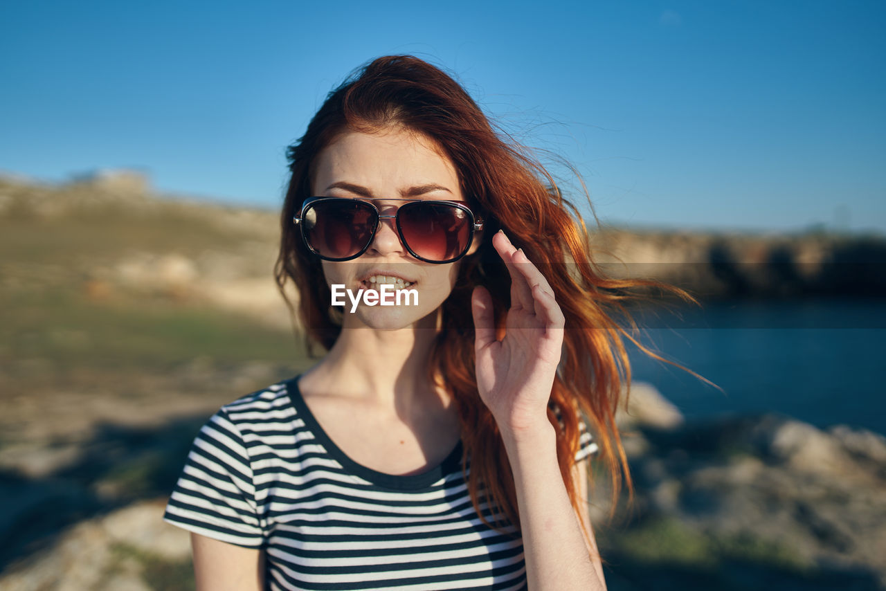 PORTRAIT OF SMILING YOUNG WOMAN AGAINST SUNGLASSES