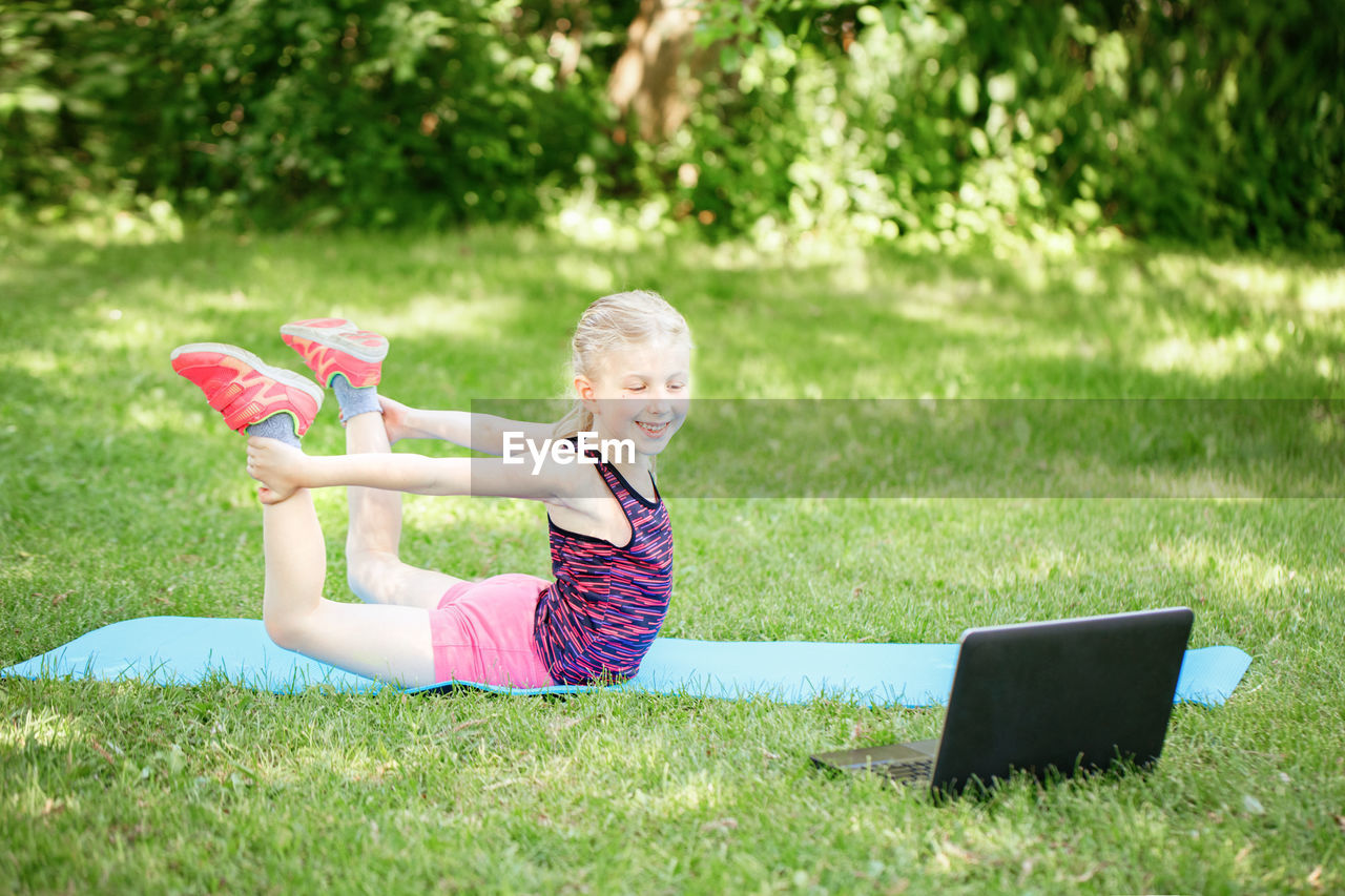 Full length of woman holding smart phone while sitting on grass