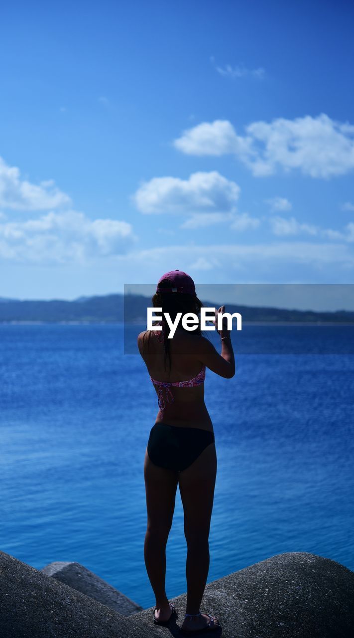 Woman standing on rock looking at sea against sky