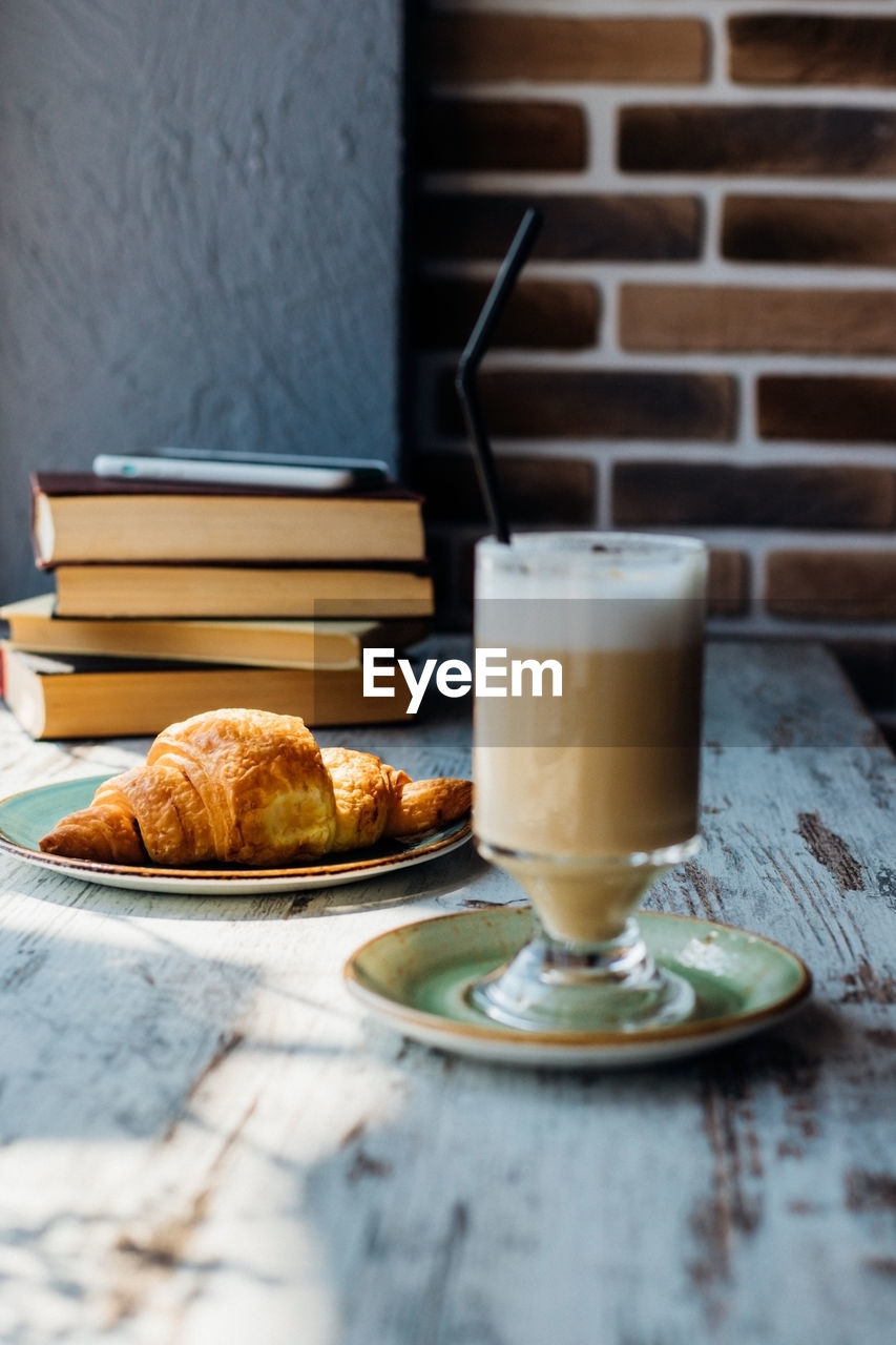 Latte in a tall glass against the background of a stack of books.the drink is on the table in a cafe