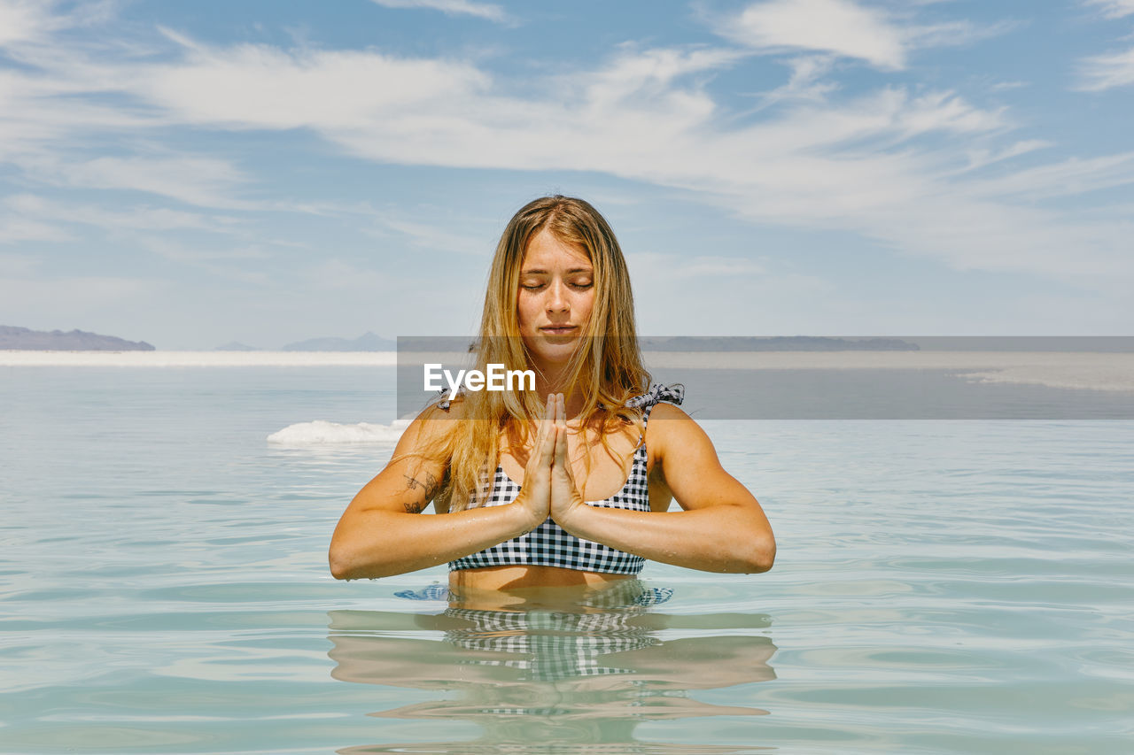 Young woman meditating in water in bonneville salt flats.