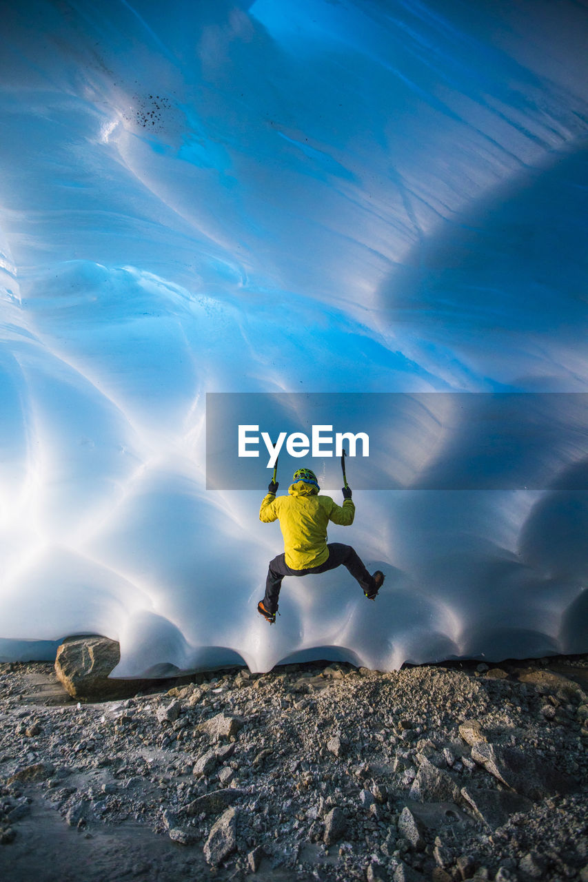 Rear view of man ice climbing in glacier cave.