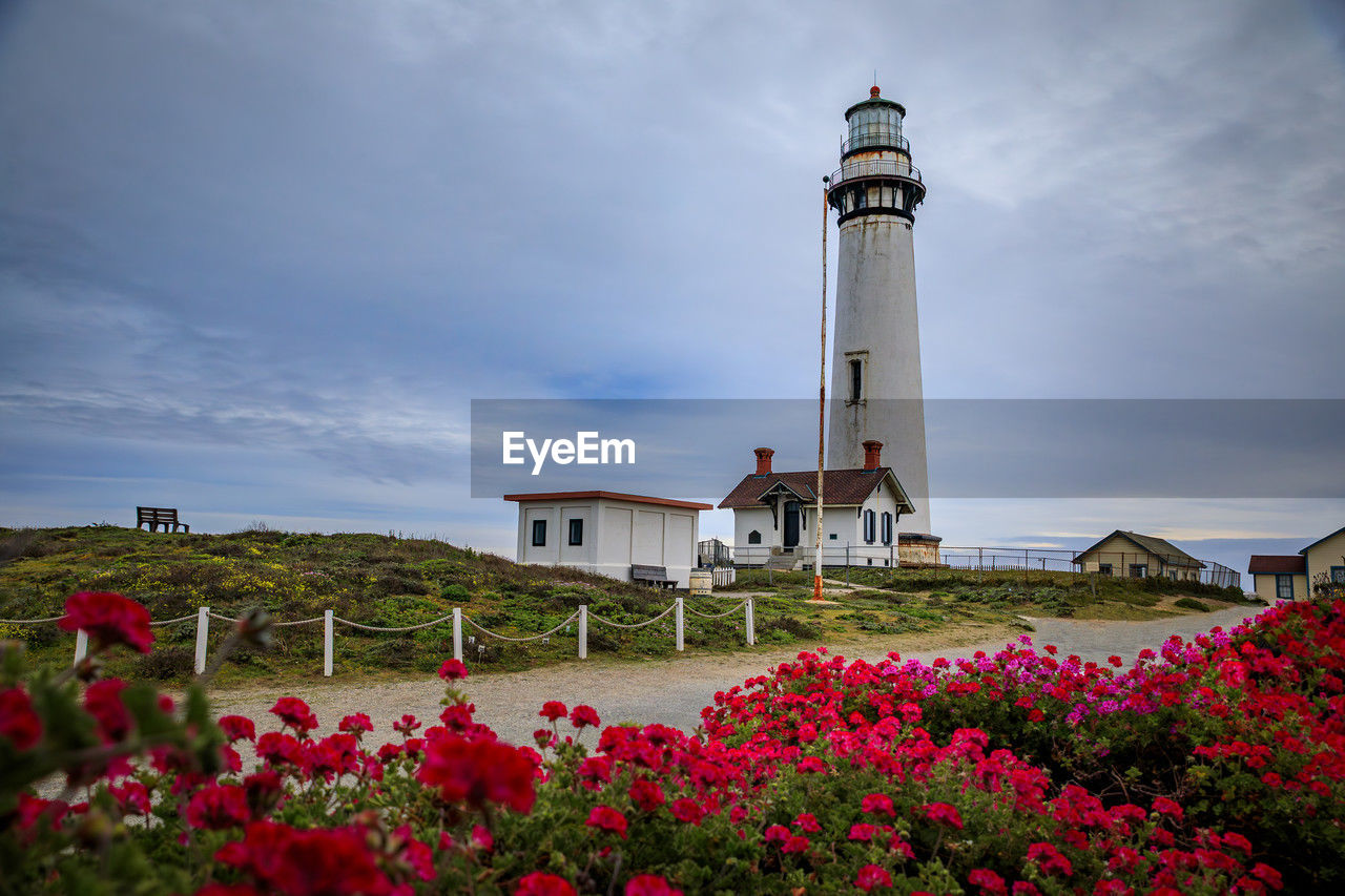 lighthouse by sea against cloudy sky