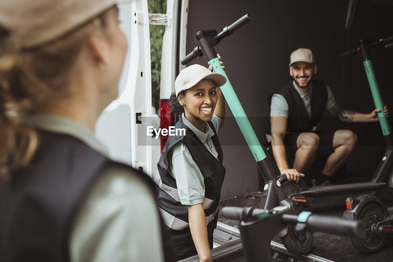 Happy female and male coworkers loading electric push scooter in delivery van