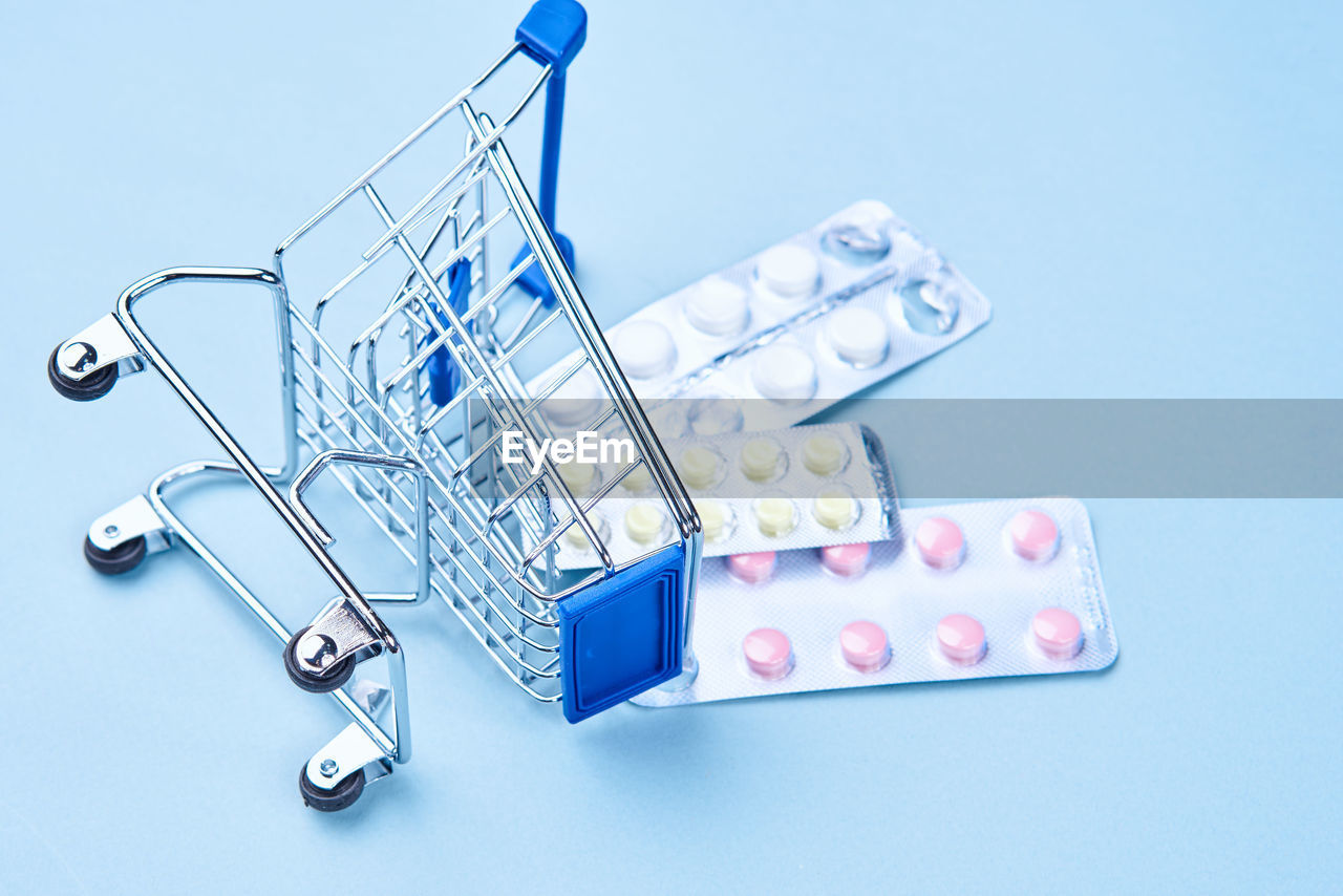 High angle view of pill spilling from shopping cart over blue background