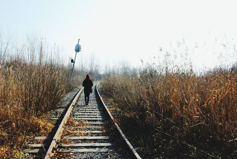 REAR VIEW OF MAN STANDING ON RAILROAD TRACKS