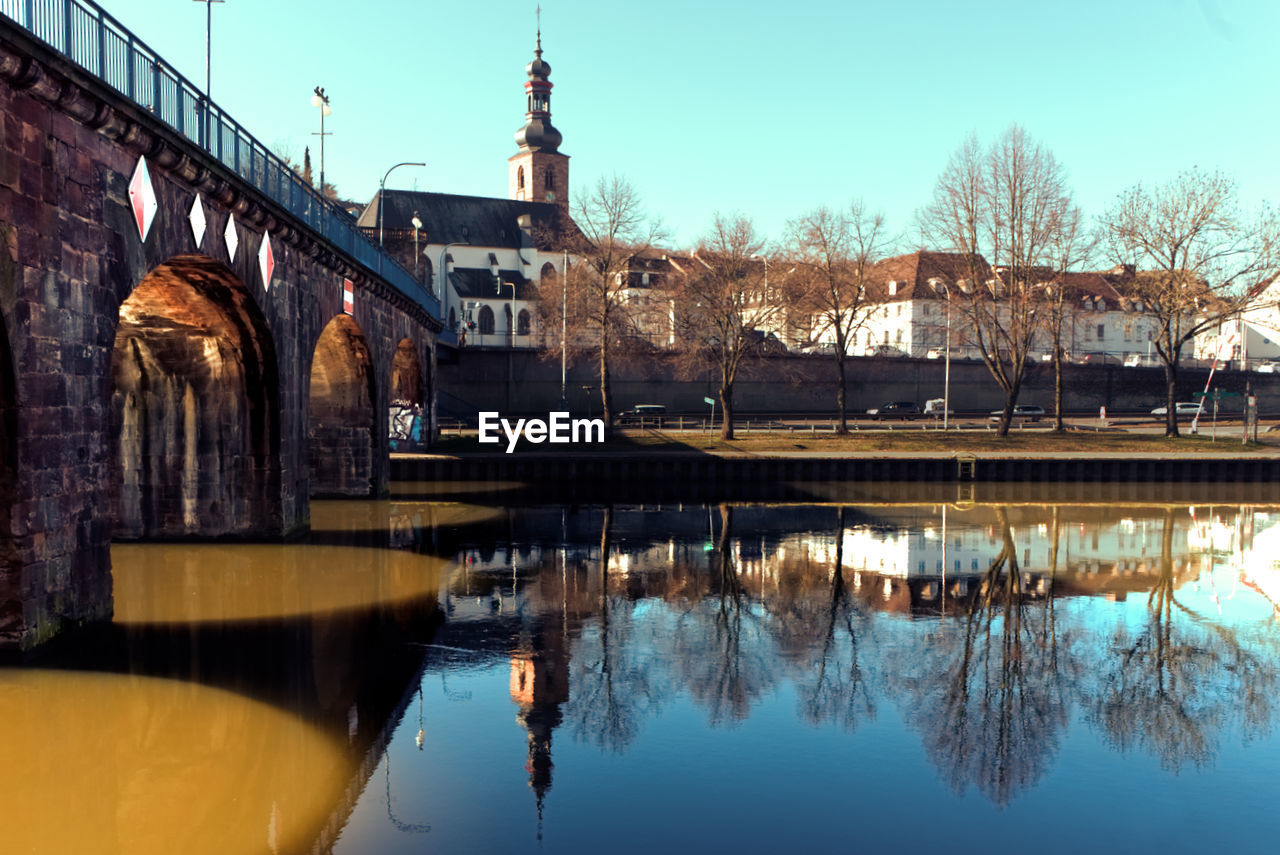 Bridge over river by buildings against sky