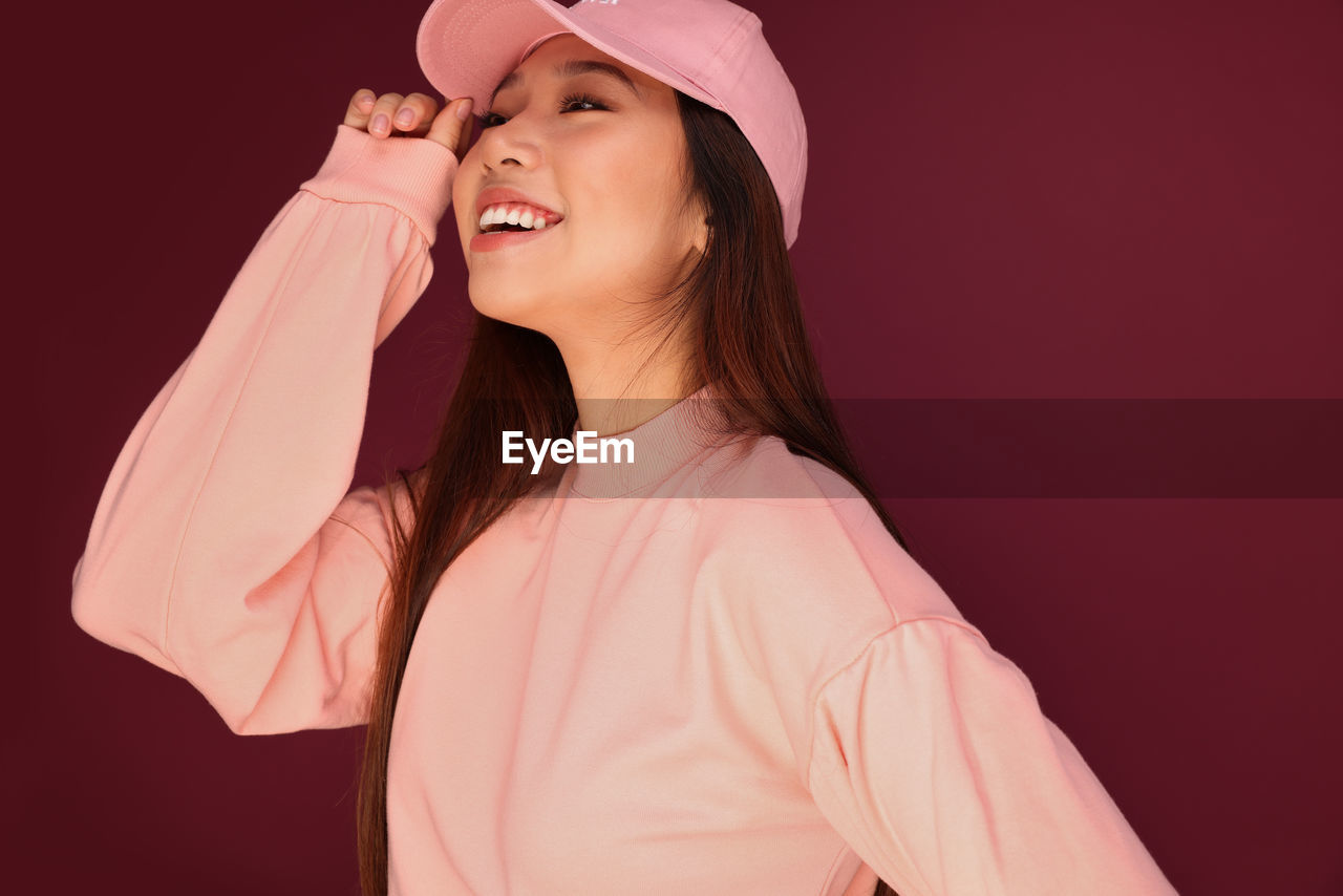 Portrait of happy young asian woman in the studio wearing pink clothes over garnet background