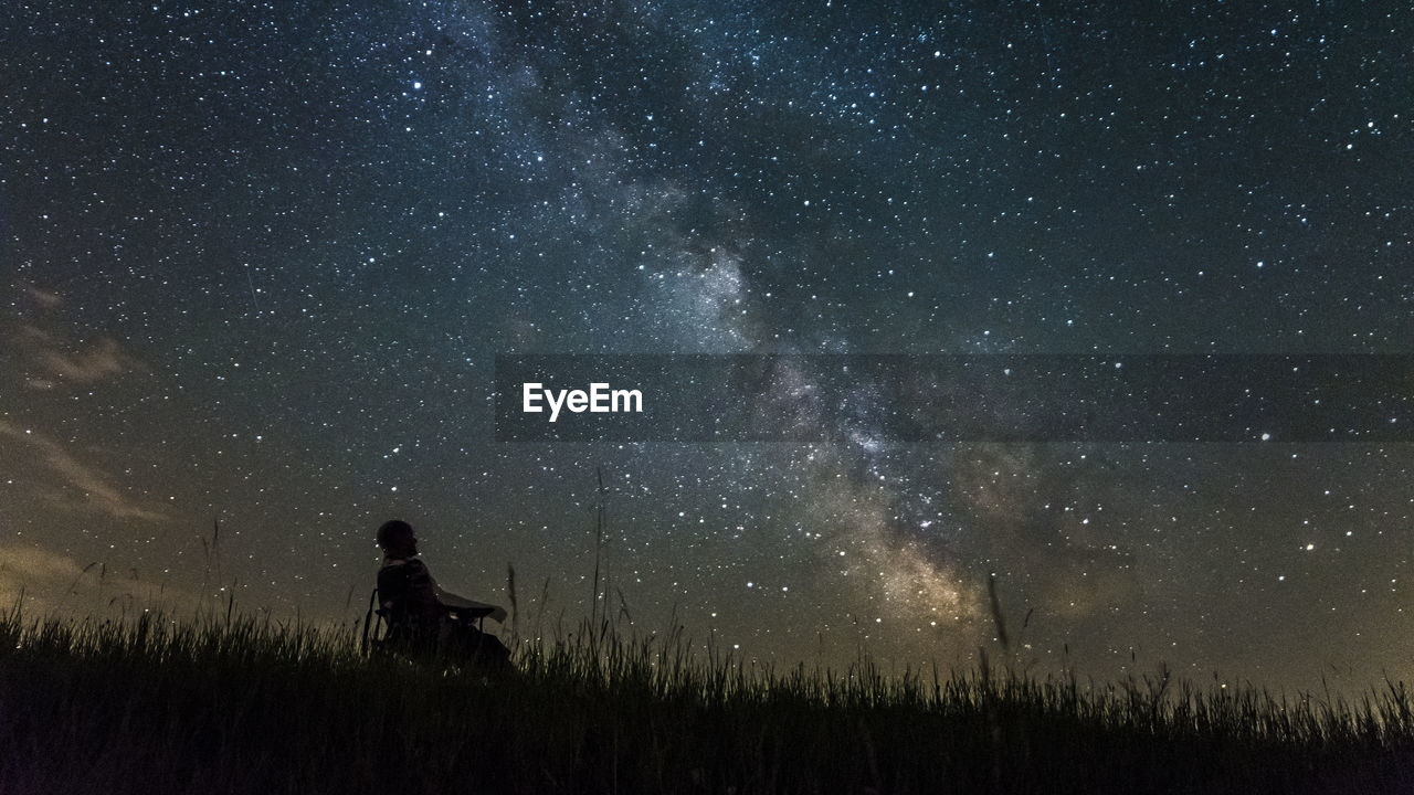 Low angle view of person sitting on field against star field