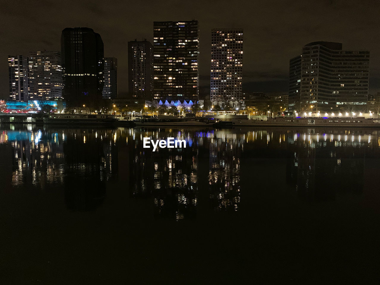 ILLUMINATED BUILDINGS BY RIVER AGAINST SKY AT NIGHT