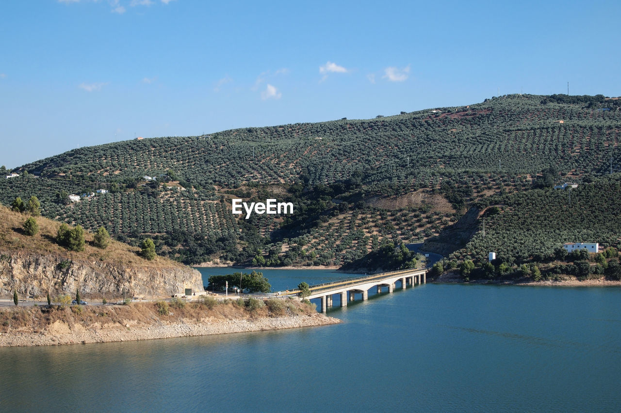 Scenic view of river by mountains against clear blue sky