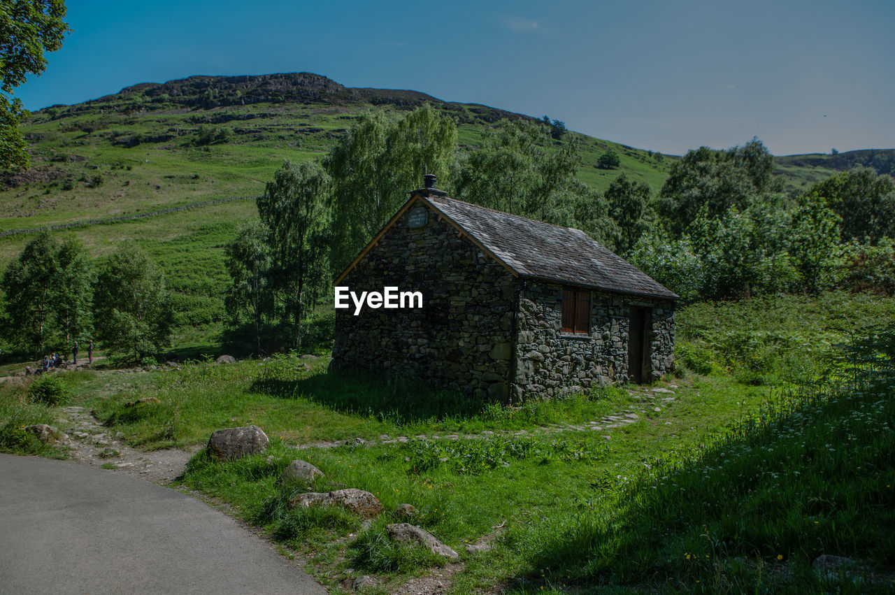 House on field by mountain against sky