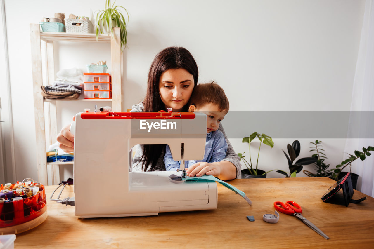 Mother with kid using sewing machine at home